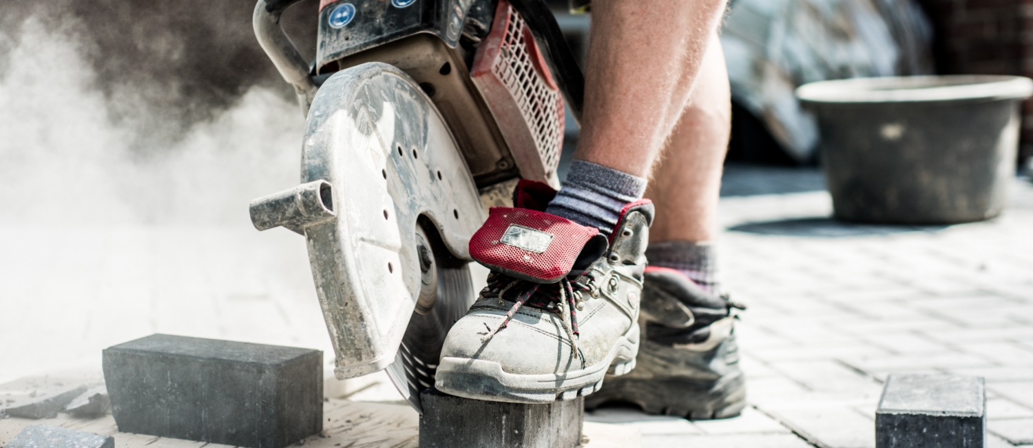 Professionelle Pflasterreparatur und Anpassungsarbeiten: Handwerker beim präzisen Zuschnitt eines Pflastersteins mit einem Trennschleifer für passgenaue Ergebnisse.