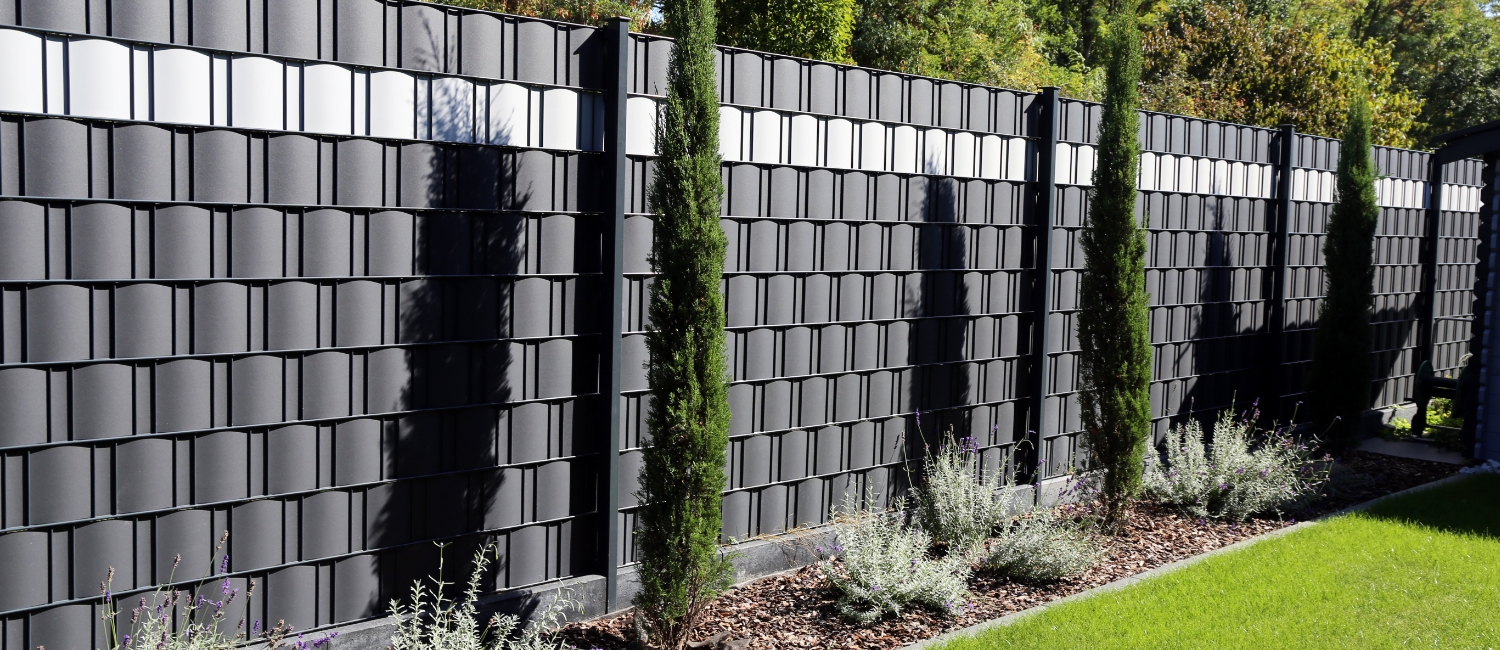 Hochwertiger Sichtschutzzaun im Garten: Doppelstabmattenzaun mit eingeflochtenen Sichtschutzstreifen in Anthrazit und Silbergrau, dekorativ bepflanzt mit Säulenzypressen und Lavendel.