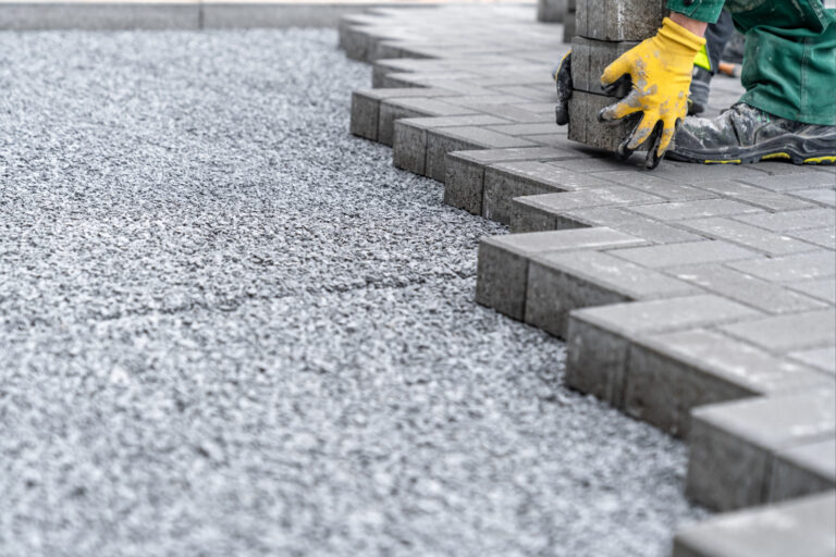 Pflasterarbeiten mit grauen Betonsteinen und Splittbett für Einfahrt.