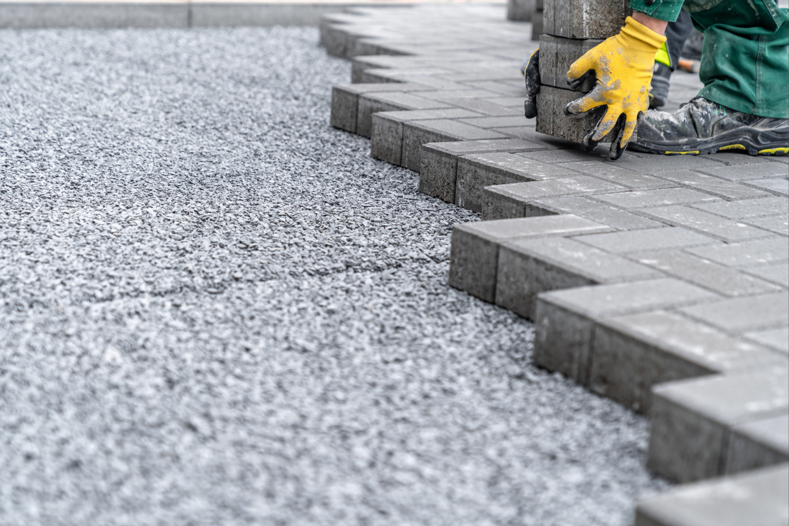 Pflasterarbeiten mit grauen Betonsteinen und Splittbett für Einfahrt.