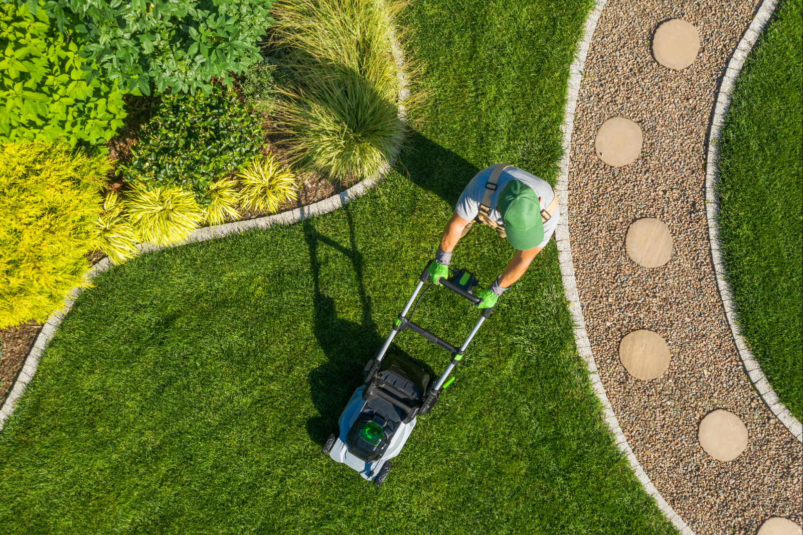 Gärtner mäht gepflegten Rasen in einem angelegten Garten.
