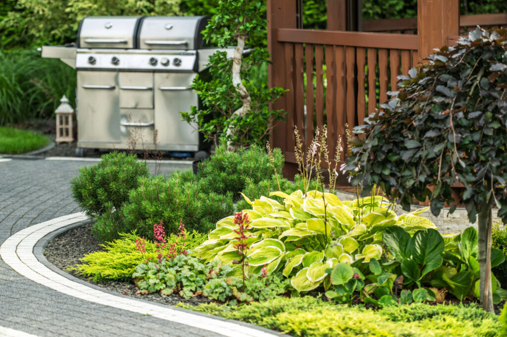 Bepflanztes Gartenbeet mit Stauden, Gehölzen, Terrasse und Grillbereich in einem gepflegten Privatgarten.