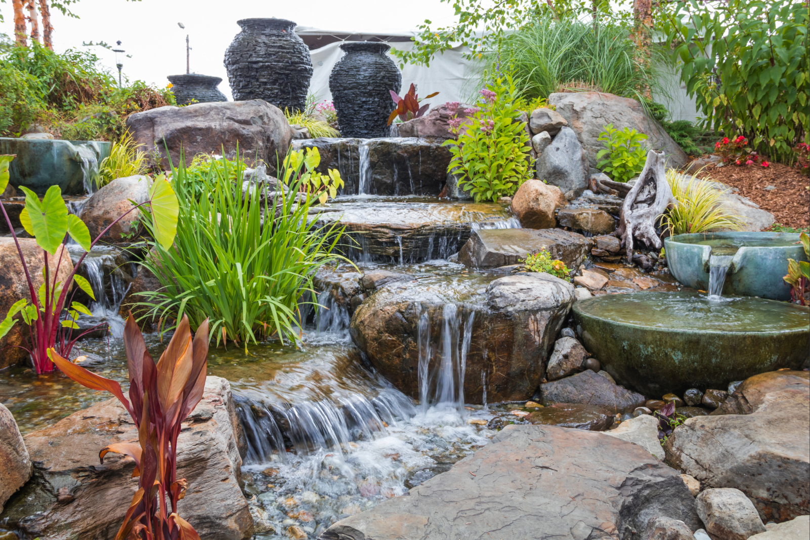 Wasserspiel mit Natursteinen, Pflanzen und kleinen Wasserfällen als Teil einer individuellen Gartengestaltung.